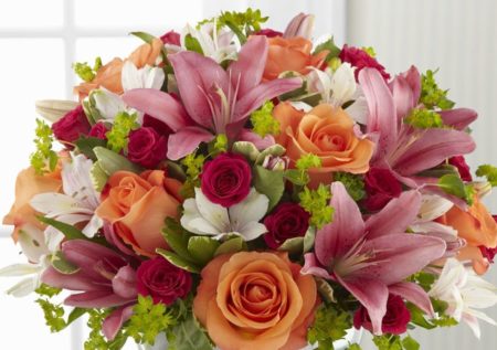 Brilliant orange roses, hot pink spray roses, pink Peruvian Lilies and pink Asiatic Lilies are accented with lush vibrant greens to create a flower bouquet full of eye-catching color and texture. Presented in a clear glass pedestal vase,