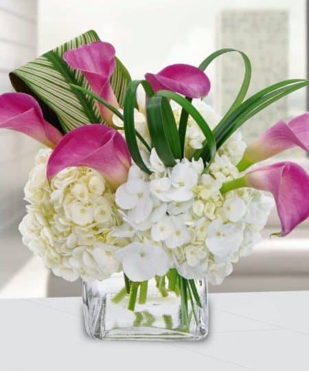  A truly one-of-a-kind, abstract, compact design featuring magnificent pink calla lilies bursting through clouds of hydrangeas in a grass cube with clear gem stones. 